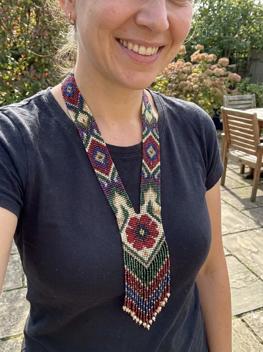 Loom-woven gerdan with a red poppy medallion and fringe, worn
