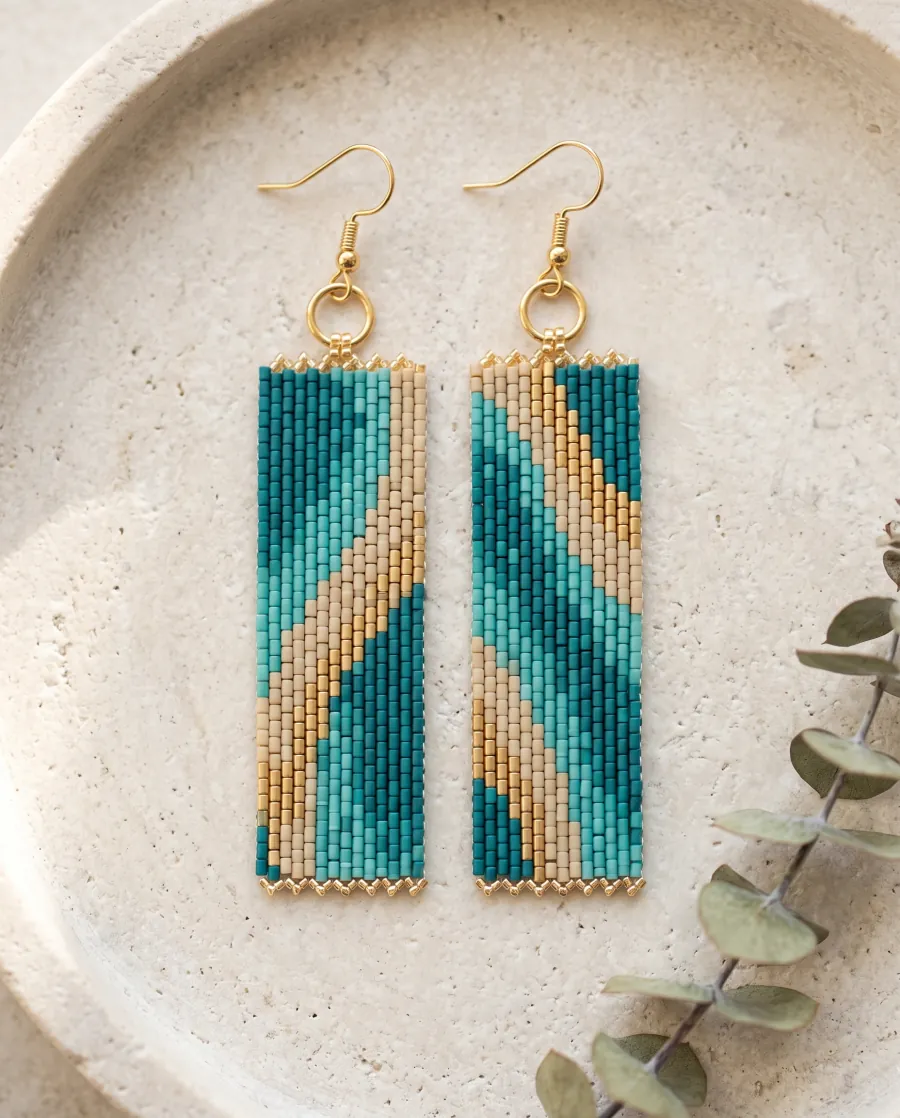 Pair of peyote stitch earrings with a teal, sand and gold diagonal wave